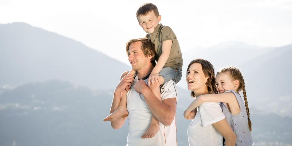 Una famiglia felice con due bambini si gode la vista sulle montagne – i genitori portano i bambini sulle spalle.